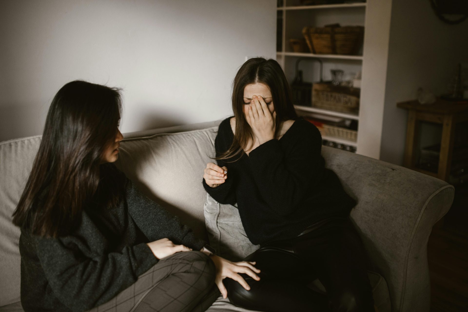 Two women having an emotional moment on a sofa indoors.